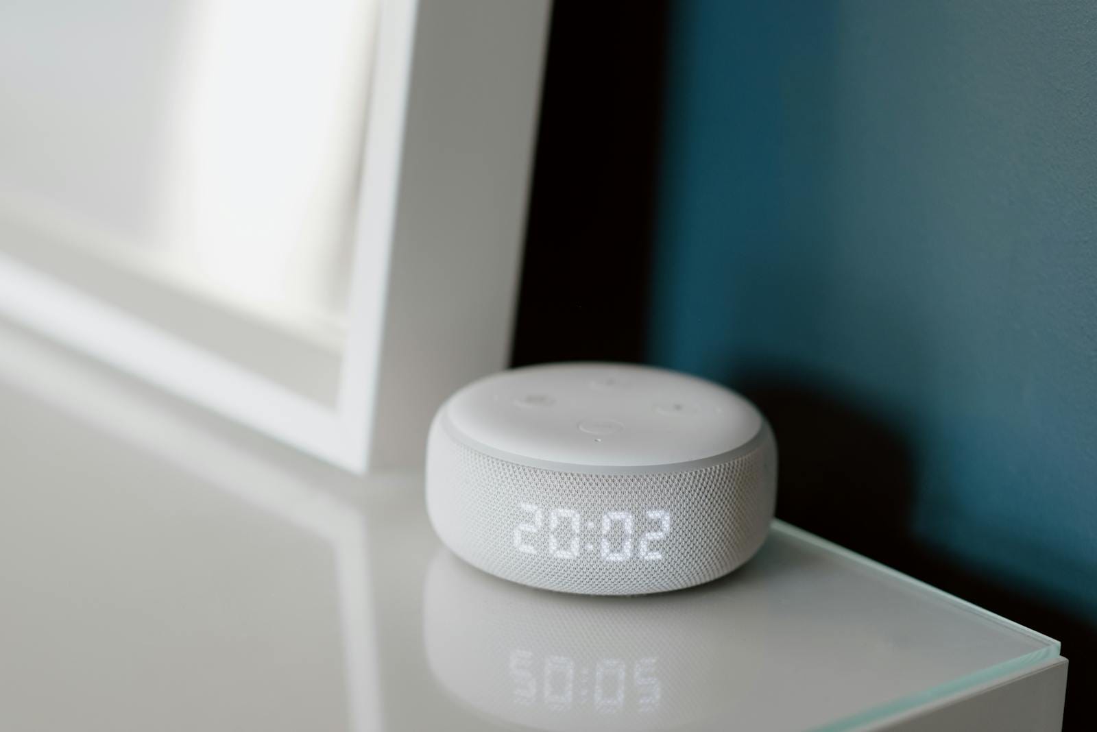 Close-up of a smart speaker with an illuminated 20:02 LED clock display on a desk.