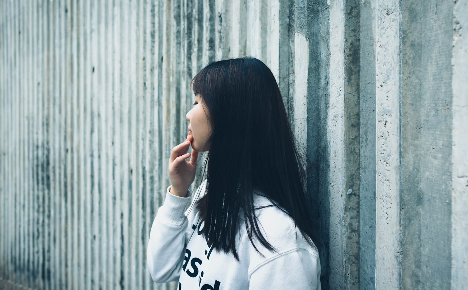 a woman leaning against a wall with her hand on her face